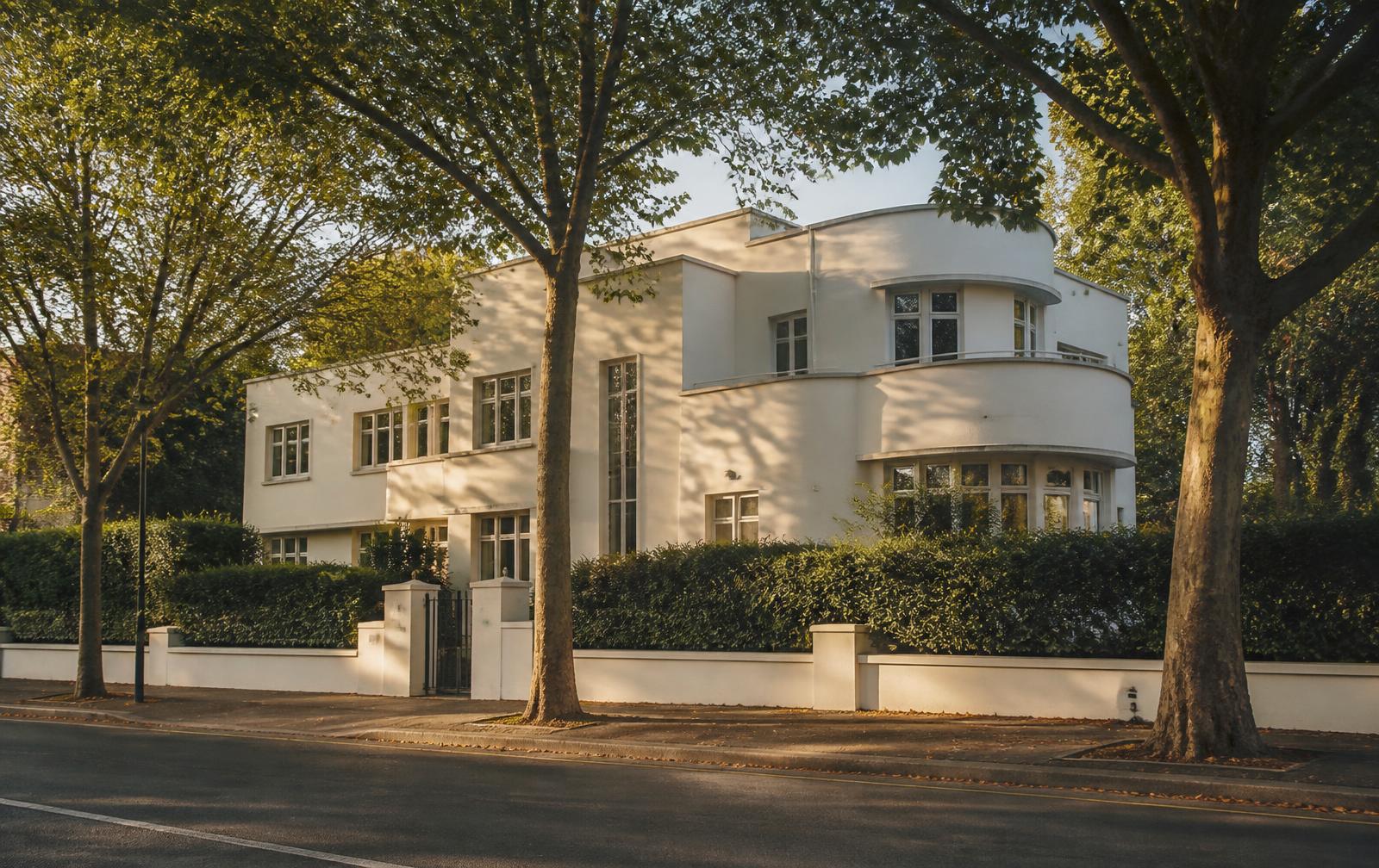 Weiße Villa der klassischen Moderne hinter geschnittener Hecke an einer baumbestandenen Allee in Düsseldorf-Golzheim im Abendlicht