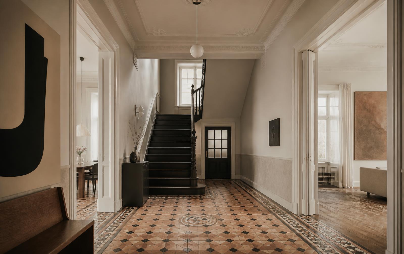 Restaurierter geometrischer Mosaikboden in einem Düsseldorfer Altbauflur mit Stuckdecke und dunkler Treppe