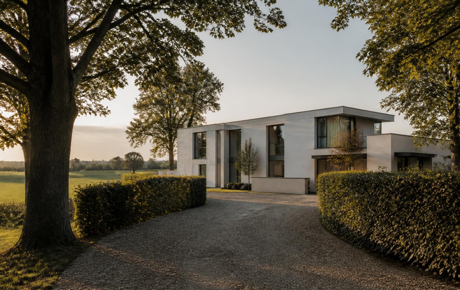 Zurückhaltende weiße Villa mit Flachdach hinter hoher Hecke, Kiesauffahrt und altem Baumbestand am Feldrand in Düsseldorf-Wittlaer